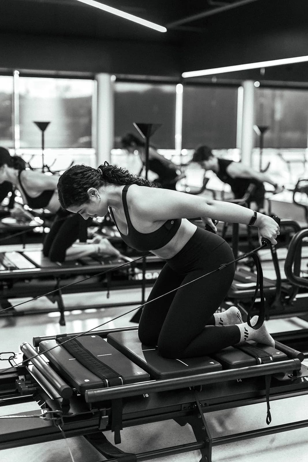 A person kneeling on a Megaformer and leaning forward with straps